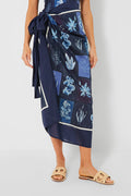 Someone wears a navy blue tropical-print wrap skirt from AGUA BY AGUA BENDITA, styled with tan open-toe sandals.