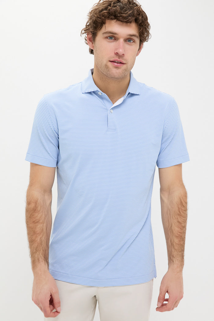 A man wears a light blue Peter Millar Performance Jersey Polo with moisture-wicking, short sleeves, and light-colored pants.