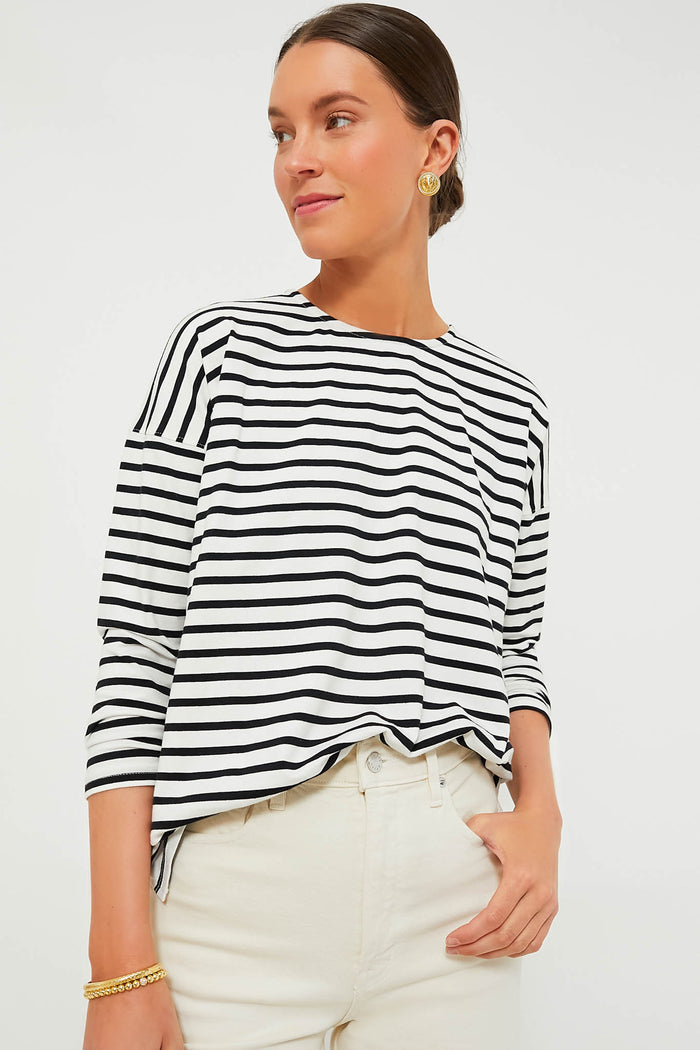 A woman wearing a Tuckernuck black and white Breton striped top and white pants stands with one hand in her pocket.