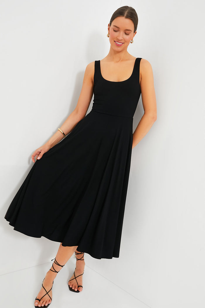 A woman wearing the Pomander Place Black Leon Dress, an elegant midi with a fitted bodice and A-line skirt, looks down as she gently holds the hem.