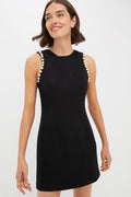 Wearing a sleeveless Hyacinth House Black & Pearl Meredith Blake Dress with pearl armhole detailing, a woman stands elegantly.