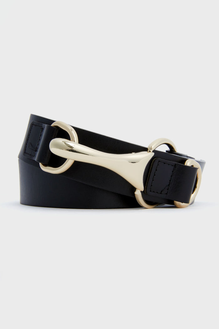The Tuckernuck Accessories Black Snaffle Belt, made from black leather, features a gold buckle and horsebit hardware, elegantly coiled to showcase its signature ring details.