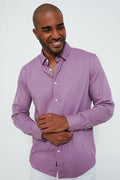 A man wearing a long-sleeve, button-up, pink and blue striped Supima cotton shirt from Faherty smiles and looks to the side.