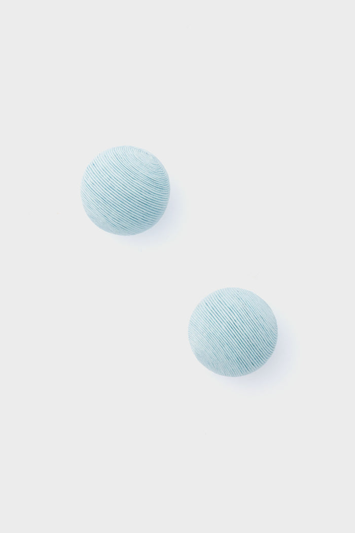 Two round, light blue, textured pieces from Tuckernuck Jewelry—reminiscent of Casey Studs or blue silk earrings—are artfully displayed.