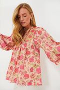 A woman wears the Mille Desert Bloom Charlie Blouse, a pink floral cotton top with long, loose sleeves, styled with white pants.