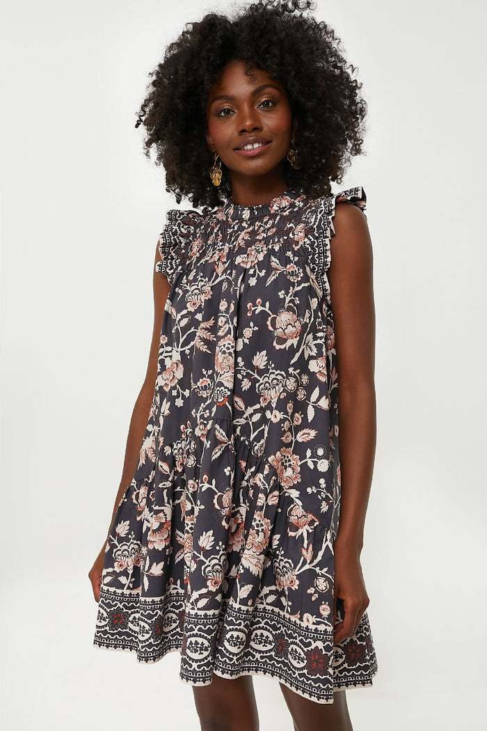A woman wears the Love the Label Viola Dress—a navy blue, cotton floral mini dress with ruffled shoulders.