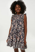 A woman wears the Love the Label Viola Dress—a navy blue, cotton floral mini dress with ruffled shoulders.