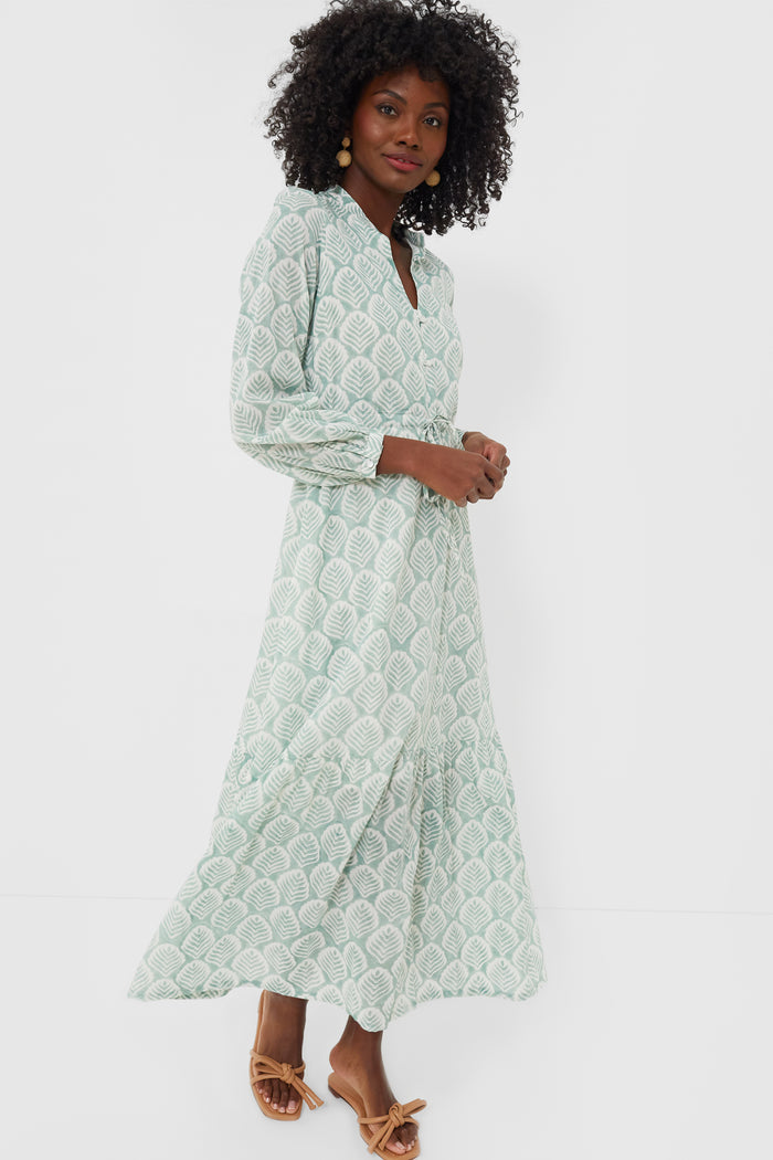 A woman wears a hand block printed, light green Love Tomas by Emerson Fry Elm Frances 3 maxi dress with a leaf pattern, long sleeves, and tan heeled sandals.