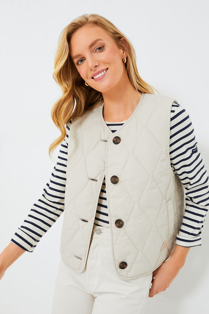 Woman wearing a cream Barbour gilet over a black-and-white striped long-sleeve shirt and light pants—a stylish, versatile outerwear choice by Barbour for any occasion.