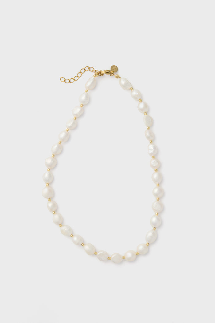 The Petit Moments freshwater pearl necklace features irregular white pearls, small gold beads, a gold clasp, and an adjustable chain for a perfect fit.