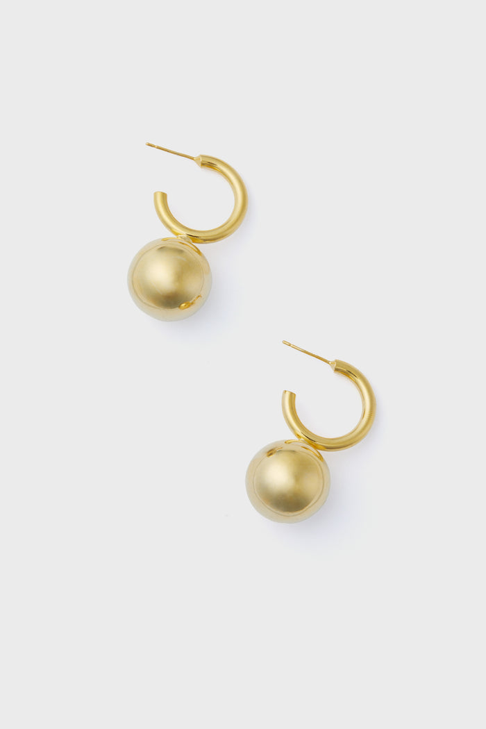 The Gold Velle Earrings by Petit Moments are gold hoops with large spherical charms, crafted by an environmentally conscious Los Angeles brand.