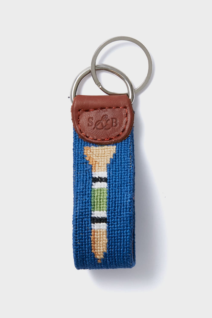 This blue needlepoint key fob by Smathers and Branson features a hand-stitched golf tee and ball design, brown leather accent stamped with S&B, and includes two metal key rings.