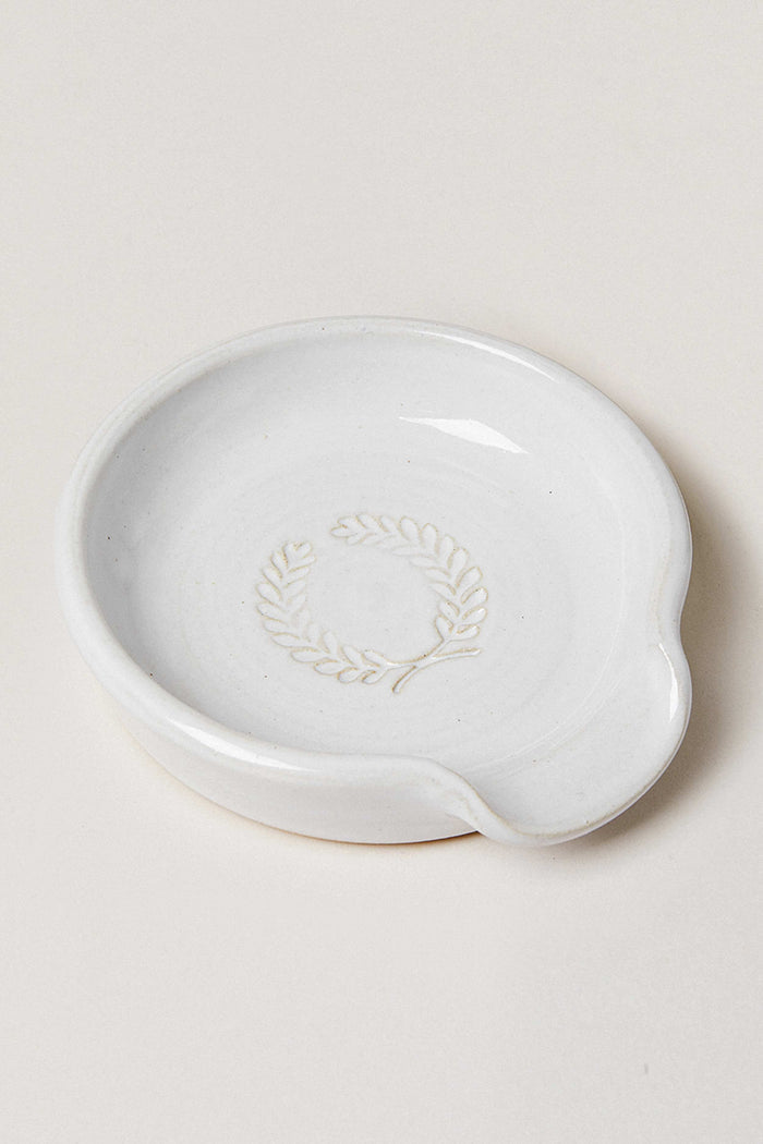 This small white ceramic spoon rest by Farmhouse Pottery, Inc features a spout and an embossed laurel wreath design—perfect for bringing classic farmhouse charm to your kitchen.