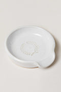 This small white ceramic spoon rest by Farmhouse Pottery, Inc features a spout and an embossed laurel wreath design—perfect for bringing classic farmhouse charm to your kitchen.