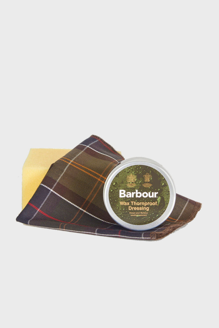 A Barbour Wax Thornproof Dressing tin, a yellow sponge, and a brown plaid cloth—ideal for caring for and reproofing your Barbour wax jacket—are neatly presented.