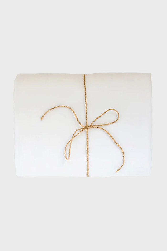 A folded white Madame de la Maison linen tablecloth, tied with a simple brown string bow and crafted from sustainable flax linen.