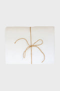 A folded white Madame de la Maison linen tablecloth, tied with a simple brown string bow and crafted from sustainable flax linen.