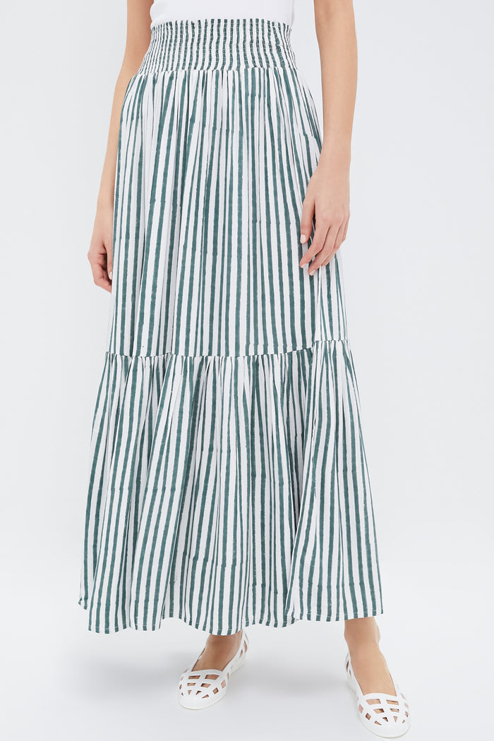 Person wearing a Love Tomas by Emerson Fry white and green vertically striped tiered maxi skirt, paired with a white sleeveless top and white cut-out flat shoes.