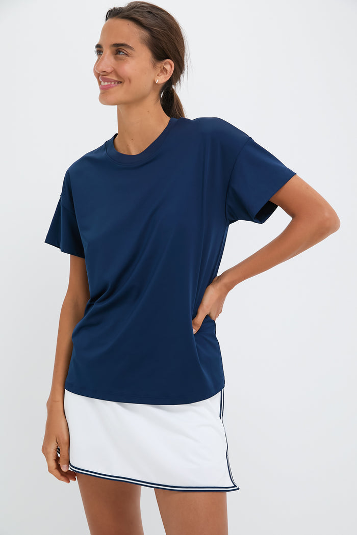 A woman in a Tnuck Sport navy blue crewneck t-shirt and a white skirt with navy trim smiles while looking to the side.