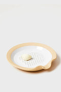 A peeled garlic clove rests on a Farmhouse Pottery, Inc stoneware grater dish with a beige rim.