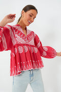 A woman poses in a loose-fitting red Oliphant bohemian blouse with white geometric and floral embroidery, paired with light-wash jeans.