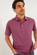 A man wears a Peter Millar short-sleeved red and blue striped performance jersey polo with UPF 50+ protection, looking up with hands in his pockets.
