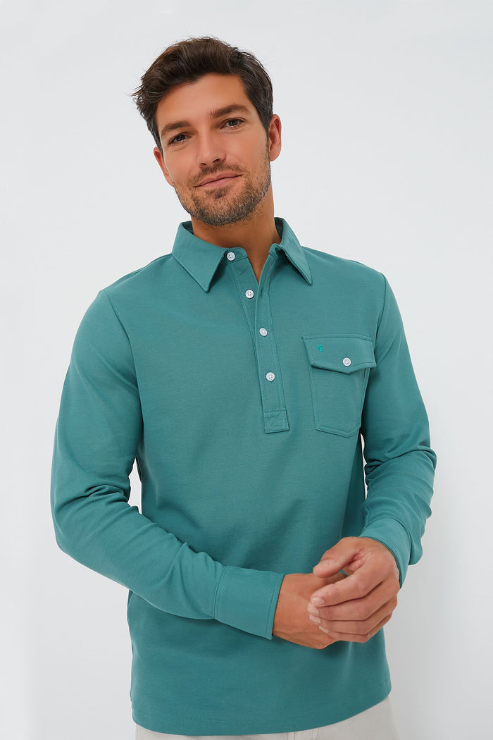 A man stands against a plain white background wearing a teal Criquet Long Sleeve Players Shirt crafted from Peruvian Pima Cotton, featuring a chest pocket.