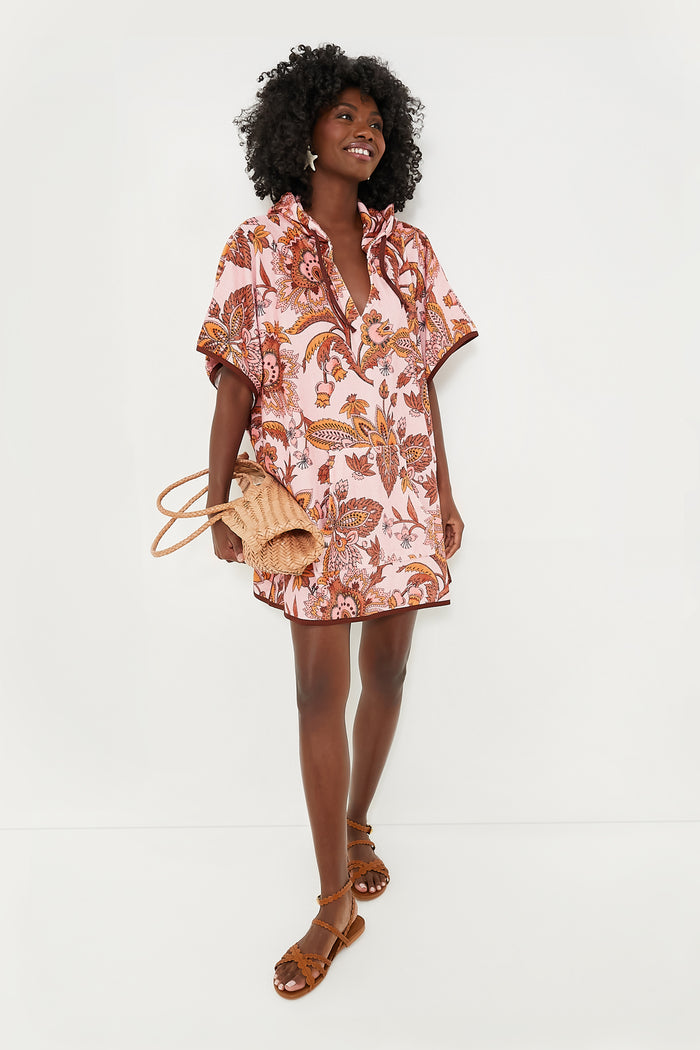A woman in a relaxed-fit pink floral print Tnuck Beach caftan, brown sandals, and carrying a woven bag stands confidently.