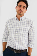 A man in a Peter Millar sport shirt with a blue plaid pattern, dark pants, and a black belt stands confidently, exemplifying refined luxury menswear.