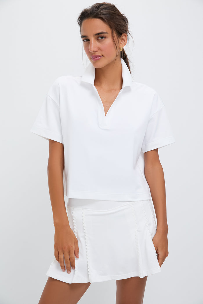 A woman wears a Tnuck Sport White Cropped Caroline Polo made from quick-dry fabric and a white skirt, both offering UPF 30 protection.